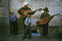 In a backstreet of the colonial town of Oaxaca stands a local family playing traditional Mexican music to an eclectic group of enthusiastic passer-bys. The father seems to be leading the musical band...