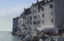 Old city waterfront building with a washing line hanging from shuttered windows and people sitting outside under the sun awning of a Pizzeria restaurant attached to the bottom of the building. Large s...