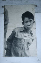 Tuol Sleng Museum. Photograph of a young male prisoner in a Khmer Rouge prison wearing a number tag around his neck