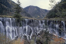 Jiuzhaigou Nature Reserve multi level waterfalls with tree covered mountains behindOctober