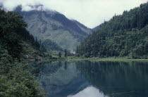 Jiuzhaigou Nature Reserve. Lake surrounded by green tree covered mountains with reflections on water