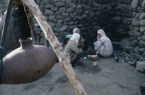 Women sitting on ground beside suspended vessel used to churn milk.Eurasia