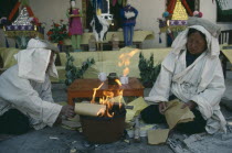 Symbolic paper money burnt at Taoist funeral with close relatives wearing white shrouds to indicate mourning.