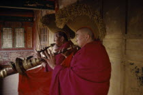 Tibetan Yellow Hat Buddhists playing long trumpet horns know as Dung Chen. Monastery of Lamas
