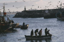 Seagulls circling above fishing boats in fortified harbour.