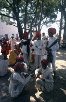 Group of men in shade of tree during midday heat at annual fair.