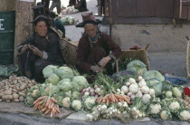 Women wearing traditional hats selling vegetables at market.