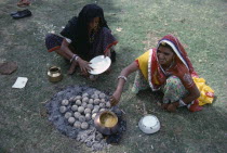 Women cooking over small open fire and hot ashes on the ground.