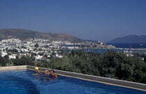 Bodrum.  People in swimming pool of Antik Theatre Hotel in foreground with view over resort to fifteenth century castle of St Peter beyond. Theater