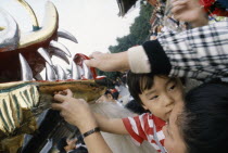 Young boy held up by his mother to touch the face of the dragon during a dragon dance