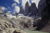 Hikers resting on hillside above a river and below towering snow capped mountains