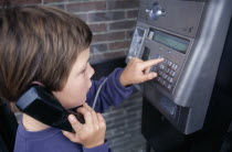 Young boy dialing on a payphone
