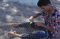 Fisherman mending net on beach.