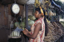 Young woman weighing bag of produce at roadside fruit and vegetable stall.scales