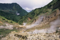 Landscape with steam rising from geysers on rocky valley floor.Windward Islands