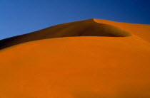 Large orange desert sand dune with a clear blue sky