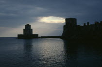 View across the sea towards fortress ruins lit by evening sun rays coming through a break in the clouds.