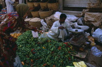 Woman buying green chilli peppers in a street market with the vendor weighing some peppers