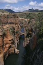 Bourkes Luck Potholes with people crossing bridge over narrow water filled canyon and mountains in the distance