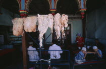 Carcasses of fat hanging outside a restaurant with people sitting at tables