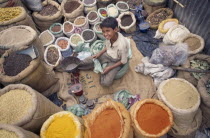 View looking down on young vendor sitting at scales in the middle of sacks of spices
