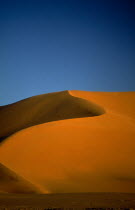 Orange desert sand dune against a clear blue sky