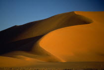Orange desert sand dunes partially cast in shadow against a clear blue sky