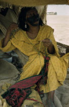 Woman embroiders a  faja  / woven woollen belt for her husband  sitting on a  fique  / cactus fibre hammock; face smeared with black fungal paint mixed with goat fat.Indigenous Tribes American Colomb...