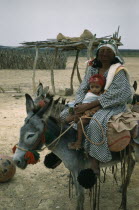 Portrait of Wayuu mother with baby daughter. Facial protection against strong sun and wind from mixture of burnt fungi and goat fat. Mother wears woollen pom-poms on feet to protect toes and as adornm...