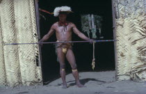 Shaman in full festive regalia � feather head-dress  red  karajuru  facial paint  dark purple  we  body dye  monkey tooth belt   cumare   fibre garters painted with yellow clay. He beats and waves the...