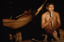 Boys playing panpipes at dusk in entrance to maloca / longhouse. One sits on an elders stool  other lies in a  cumare  / fibre hammockIndigenous Tribes  rio Piraparana North West Amazonia Amazon Amer...