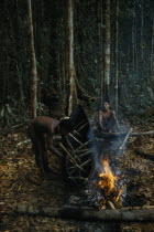 2 men making a canoe from a single tree trunk. After initial shaping with axes  canoe burnt and sides expanded in heat with wooden spacers. Burning slims sides  shapes and hardens the woodIndigenous...