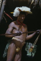 Shaman beats ceremonial  kurubeti  / stave to fend off evil spirits and thunder storms. Adorned with white egret down and macaw tail feather crown  monkey tooth belt red  karajuru  facial paint and bl...
