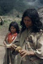 Man rubs lime encrusted gourd with ritual stick  having inserted lime  powder into a wad of coca leaves held in his cheek. Process has a ritual/sexual significance  the stick is the male penis  the g...