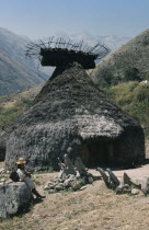 A  nuhue  / temple at ritual centre of Macotama. Granite seats placed outside temple for  mamas  / priests. Potsherds in the rack at roof apex. Young Kogi  vasayo   / commoner leans on granite boulder...