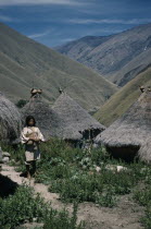 San Miguel village. A young  mama  / priest stands in pathway leading  to thatched dwellings and ritual centres  with sacred pots at roof apices.Indigenous TribesCaribbean coast of Colombia. America...