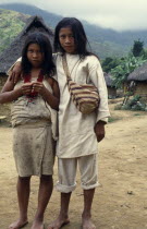 Parque Nacional. Portrait of Kogi brother and sister standing in village of Avingue with grass thatched huts behind them Wearing traditional woven cotton garments Boy has typical fique/cactus-fibre mo...