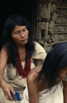 Parque Nacional. Kogi mother and grandmother sit outside family home in Avingue  Mother combs head lice out of old grandmas hair. She wears many strands of dark red glass beads  the favourite colour o...