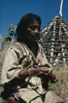 Mama/Priest Valencia takes a "coca break" - taking lime powder from his poporo/gourd to put into wad of coca leaves in his mouth - whilst thatching the roof of his house Wearing traditional thick wove...