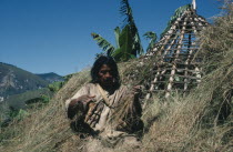 Mama Valencia a Kogi mama/priestre-thatching the conical roof of his house with recently cut hay in lowland settlement of San Antonio He wears traditional criss-crossed mochilas/ shoulder bags over a...