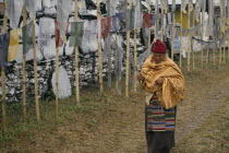 A pilgrim holding a prayer wheel  walking past a mani wall and Buddhist prayer flags.