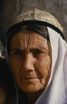 Portrait of an old woman at the Sunday market. Wearing a white head scarf and gold with black trim hat.