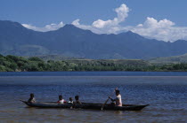 Mother ferrying her children across the bay in a Pirogue with mountains in the distance