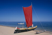 Ifaty Beach. Pirogue boat with red sail on sandy beach next to the waters edge