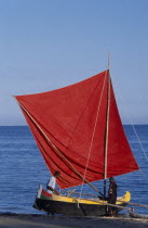 Ifaty Beach. Men with a red sail Pirogue boat at the waters edgeA pirogue is a small flat hulled boat of a design associated particularly with West African fishermen