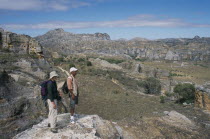 Tourist and guide standing on edge of rock looking over craggy sandstone massifs