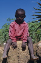 Near Ambositra. Portrait of a young child wearing a red hooded top sitting on a wall