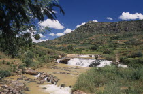 Road to Antsirabe. River and waterfall running between green landscape with buildings set into the hillside