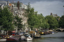 Canal and moored houseboats and barges overlooked by traditional architecture. Netherlands