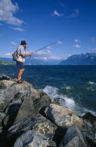 Fisherman standing on rocks at the entrance to Lutry Marina.